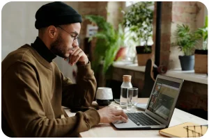 Homme concentr&eacute; travaillant sur un ordinateur portable dans un caf&eacute; cosy avec des plantes.